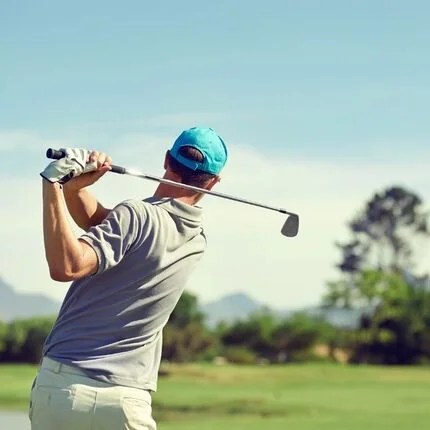 A man hitting a golf ball on a green field with a blue sky in the background